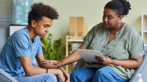 Psychologist working with teenage boy at office African psychologist supporting depressed teenage boy feeling guilty about behavior during therapy at office